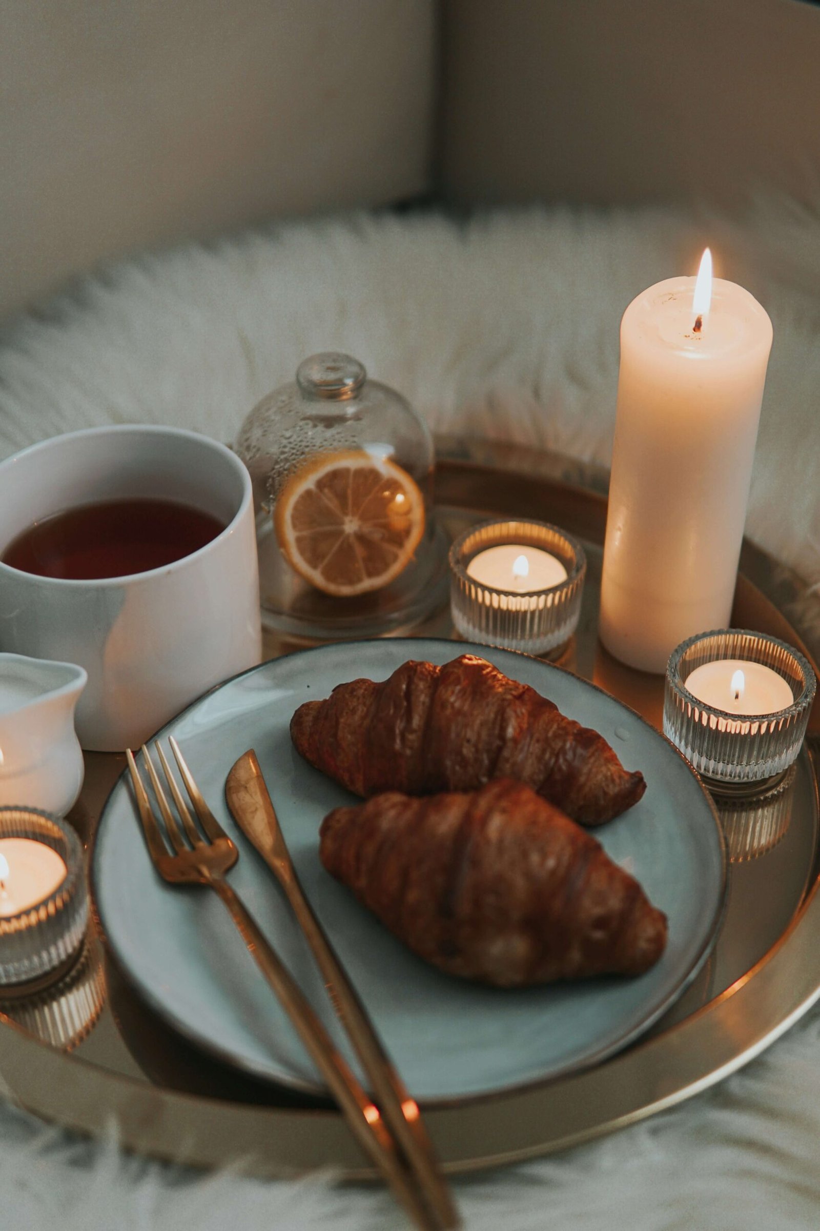 Warm and cozy breakfast setup with croissants, tea, candles, and citrus slices.