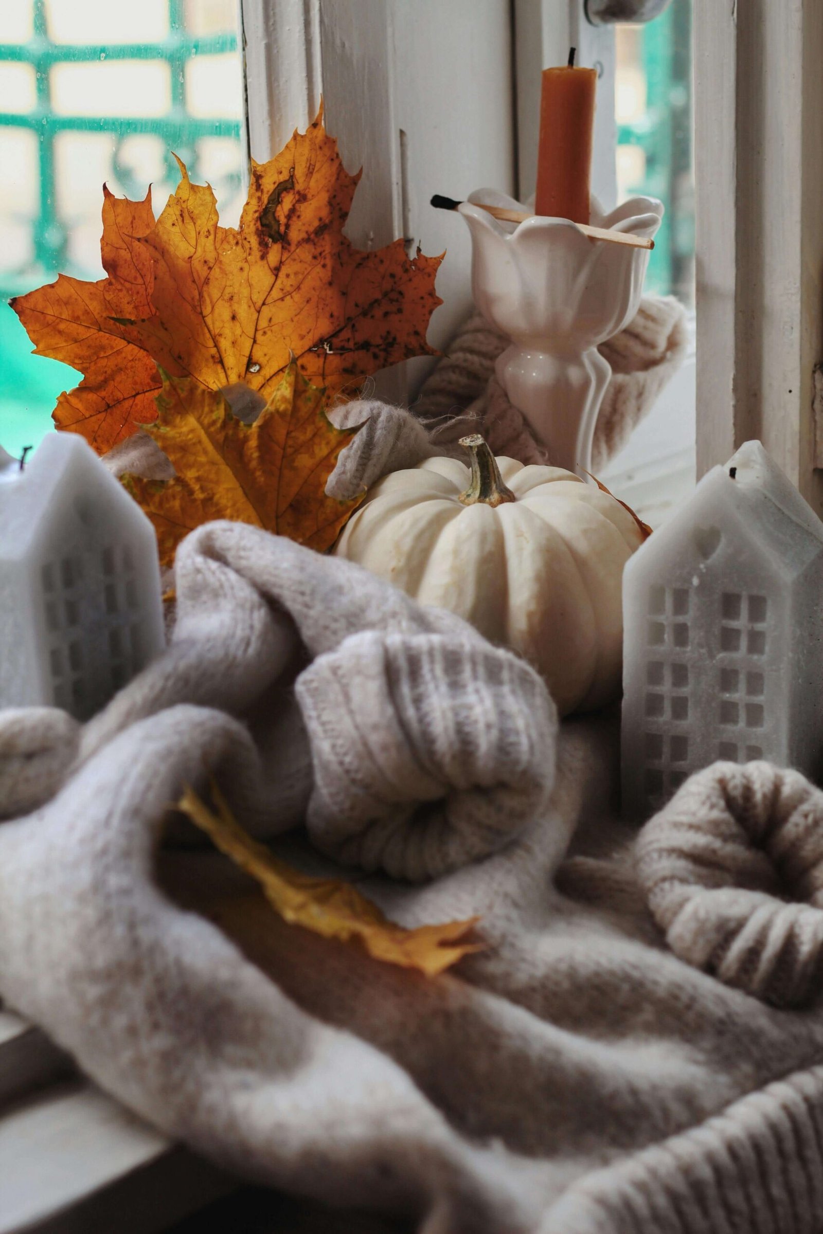 Autumn-themed cozy setup with pumpkins, leaves, and knit accessories near a window.